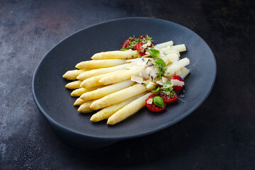 Weißer Spargel glasiert mit Kirschtomaten und Parmesan Käse serviert als close-up auf einem Design Teller mit Textfreiraum