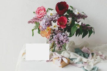 Happy Mothers day. Greeting card mock up and stylish bouquet with gift box and pastel ribbons on wooden table in modern rustic room. Space for text. Happy Womens day. Postcard mockup