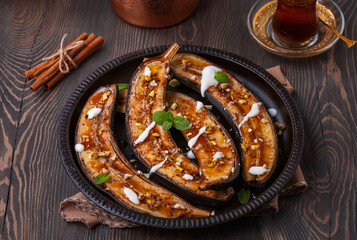 Baked Bananas. Banana halves baked with maple syrup and cinnamon topped with yogurt and chopped nuts. Dark wooden table, selective focus, horizontal.
