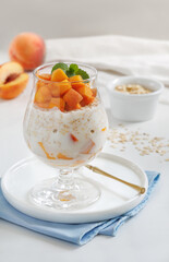 Peaches and Cream Overnight Oats. Healthy breakfast made with oats soaked for the night in milk or yogurt layered with cubes of fresh peaches, served in a clear glass. Selective focus, vertical.