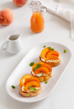 Peach Crostini with crumbled cheese, honey and mint on a plate with fresh peaches and bottle of juice on background. Selective focus, vertical.