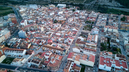 Naklejka premium Aerial view of a lively Spanish city with red-roofed buildings, narrow streets, mountains, and buildings of varying height and style.