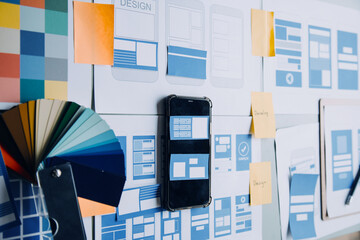 Close up ux developer and ui designer brainstorming about mobile app interface wireframe design on table with customer breif and color code at modern office.Creative digital development agency