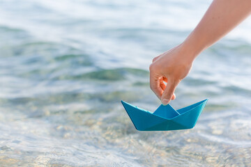 hands of a young woman with a paper boat by the sea in summertime