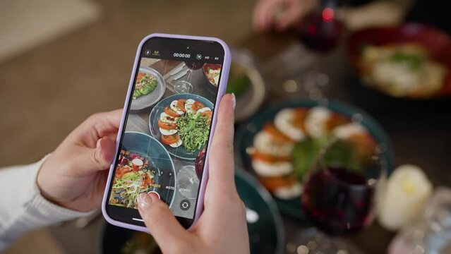 Close-up woman's hands take food by phone. Close-up of a woman's hands using a smartphone to take a photo of food. Female hands take a picture on a smartphone eating fresh tomato salad for lunch.