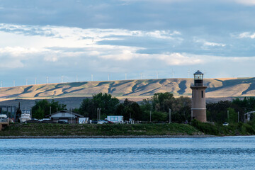 A lighthouse on a river, in the distance wind turbines can be seen atop the hills.