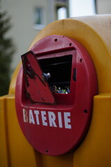 Zbliżenie na uchylone drzwi zbiornika na zużyte baterie wbudowanego w większy, żółty śmietnik