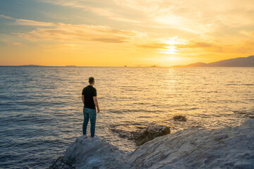Young man standing on rocky beach at sunset time  