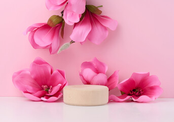 Empty round wooden platform and branches with pink magnolia flowers on a pink background. Place for demonstration of products