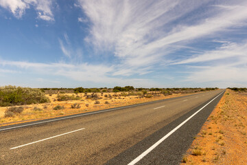 Fototapeta na wymiar australian country asphalt road stretching till the horizon through the landscape with clouds in the sky above, travel australia