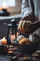 Autumn home composition with aromatic candles. Woman in wool sweater holding a pumpkin. Aromatherapy on a grey fall morning, atmosphere of cosiness and relax. Wooden dark background