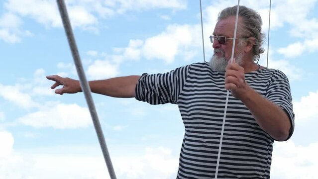 Mature Handsome sailor senior bearded man dressed in sailors shirt navy striped uniform, tells maritime stories, navigating sail boat or yacht floating in sea, sailing, age, tourism, travel and people