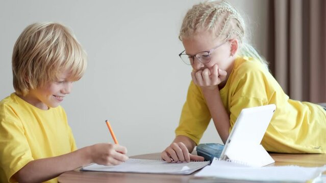 Sister helps little brother do school homework at home, Distance learning online education, boy and girl studying at home with digital tablet.
