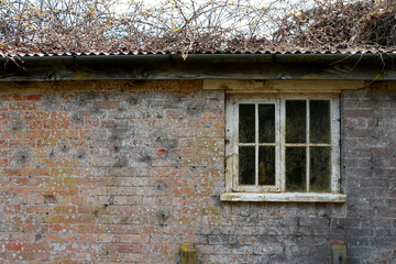 an old timber window in a run down brick built farm building with corrugated roof 