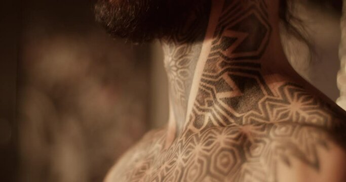 Shirtless young bearded guy standing in tattoo salon