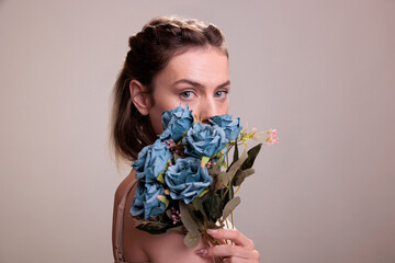 Young woman holding blue roses bouquet in front of face and looking at camera. Fashion model posing...