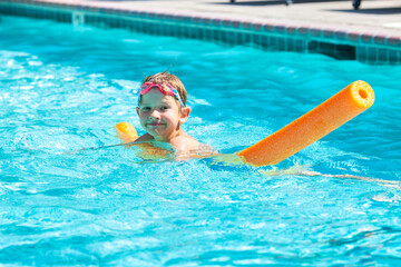 Oudoor summer activity. Concept of fun, health and vacation. Happy smiling boy five years old in swim glasses swim in the pool with noodle in hot summer day.