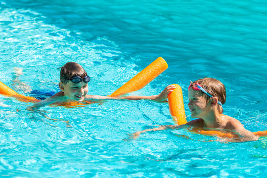 Oudoor summer activity. Concept of fun, health and vacation. Happy smiling boys eight and five years old in swim glasses swiming in the pool with noodles on hot summer day.