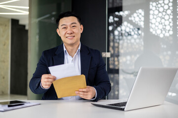 Portrait of successful businessman inside modern office building, asian man received good news news in envelope opens letter happy smiling and looking at camera.