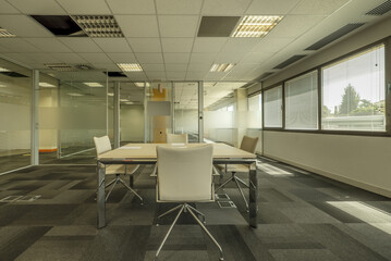 Empty offices with glass partitions, a lone desk in the center, carpeted floors
