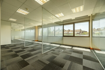 Empty offices with several glass partitions separating cubicles, long windows