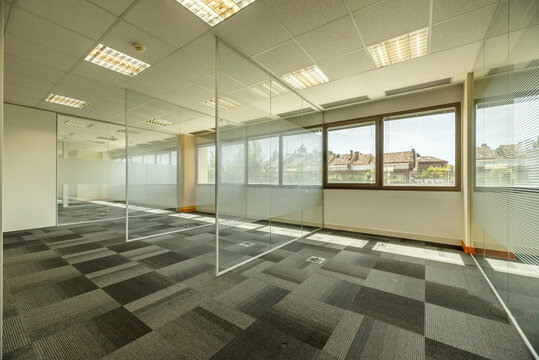 Empty offices with several glass partitions separating cubicles, long windows