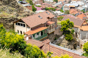 House, residential building with red tiled roof and carved wooden balconies on mountain cliff in old historic city town Tbilisi, Georgia top view. Scenic summer landscape