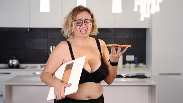 Stout woman holds pizza slice and scales making decision