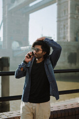 Handsome stylish guy from India calling by phone near the Tower Bridge London.