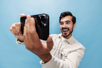 Portrait of a stylish man brunette smile and open mouth looks at the phone blogger with a beard, on a blue background in a white T-shirt and jeans, copy space