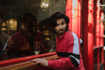 Fashion portrait of Indian Guy on the front of old building looking to the camera wearing a red shirt. Indian lifestyle and fashion. High quality photo