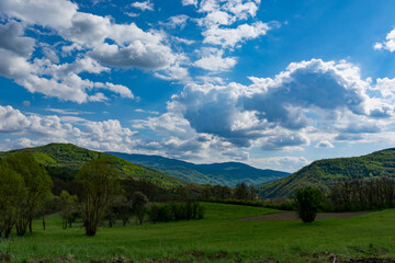 Fototapeta na wymiar A landscape of nature with sunlit hills and meadows, accompanied by white fluffy clouds in the sky on a sunny spring day