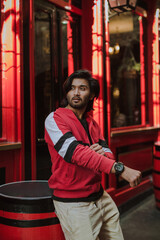Obraz na płótnie Canvas Fashion portrait of Indian Guy on the front of old building looking to the camera wearing a red shirt. Indian lifestyle and fashion. High quality photo