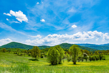Beautiful panorama with green meadows, hills in the background, and blue sky with white clouds on a spring day in nature. Natural background concept