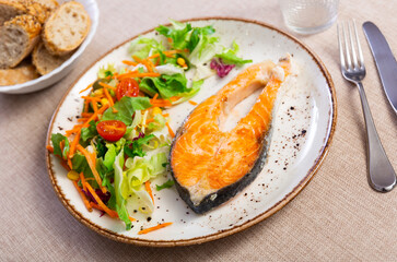 Delicious baked salmon served with lettuce and vegetables on plate