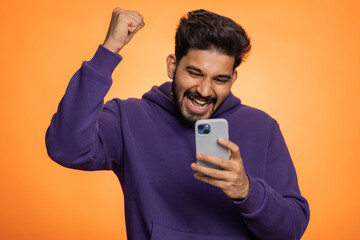 Happy excited joyful indian man in purple hoodie use smartphone typing browsing shouting say wow...