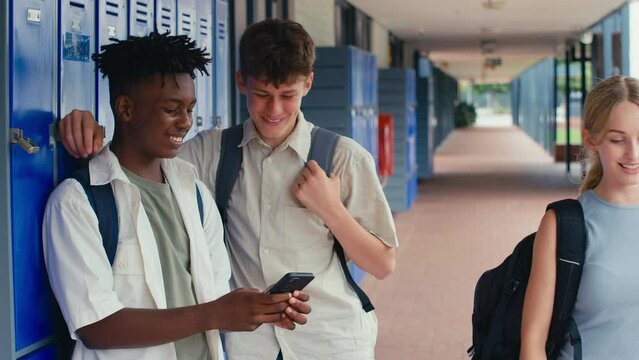 Two male high school or secondary students looking at social media or internet on mobile phone by lockers - shot in slow motion