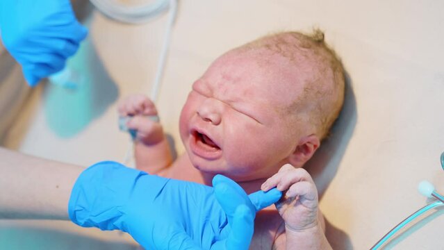 Newborn Caucasian baby cries bitterly. Medic&rsquo;s hand in latex gloves soothes the child touching the chin. Close up.