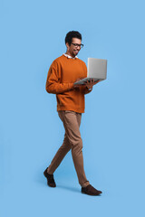 Happy man with laptop walking on light blue background