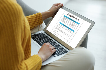 Woman filling online complaint form via laptop indoors, closeup