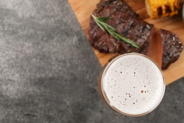 Glass of beer, delicious fried steak and corn on grey table, flat lay. Space for text