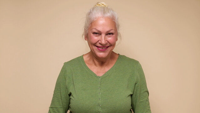 An elderly European woman in glasses confidently looks into the camera, smiling