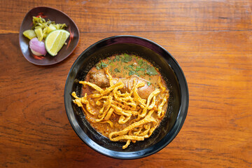 Khao Soi or Kao Soi Thai Curry Soup Noodles with Chicken and Thai spicy egg noodles on a wooden table. The delicious favorite famous Thai Food.