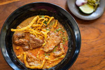 Khao Soi or Kao Soi Thai Curry Soup Noodles with braised beef and Thai spicy egg noodles on a wooden table. The delicious favorite famous Thai Food.