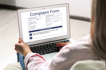 Woman filling online complaint form via laptop indoors, closeup