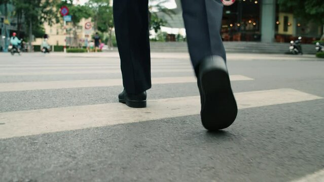 Rear view of a hurry aucasian middle aged business man in leather shoes and suit on the way to the office building,businessman in a suit crosses the road on a zebra crossing, man gets work.Slow motion