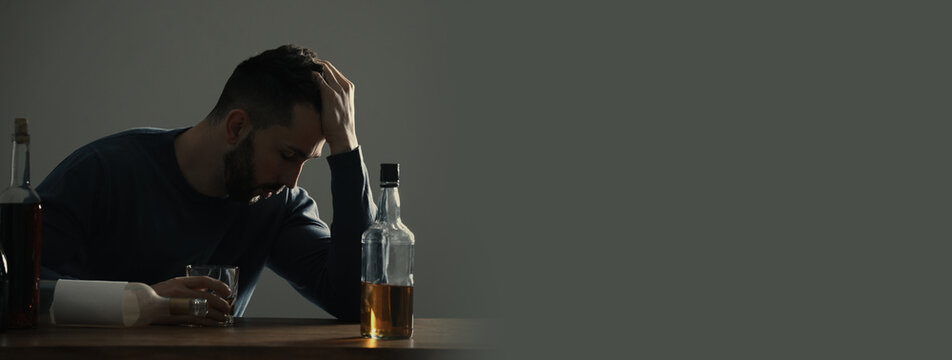 Suffering from hangover. Man with alcoholic drink at table against grey background, space for text. Banner design