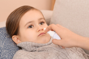 Mother using nasal spray to treat her little daughter on sofa, closeup