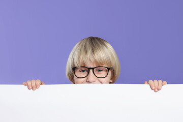 Cute little boy in glasses with blank board on purple background