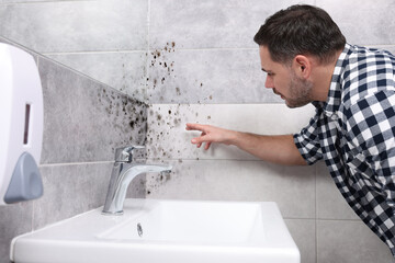 Man looking at affected with mold walls in bathroom